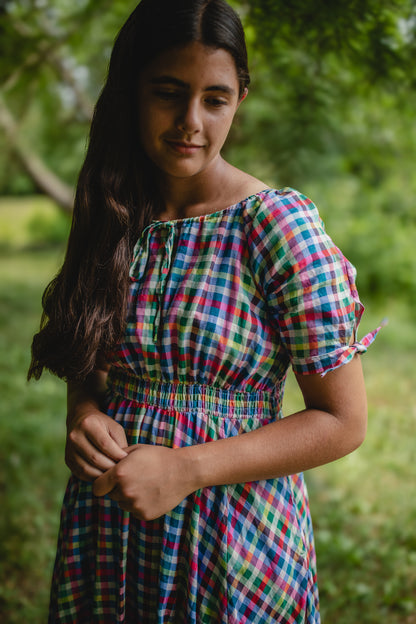 Woman wearing a colorful checkered modest nursing dress standing outdoors with greenery in the background