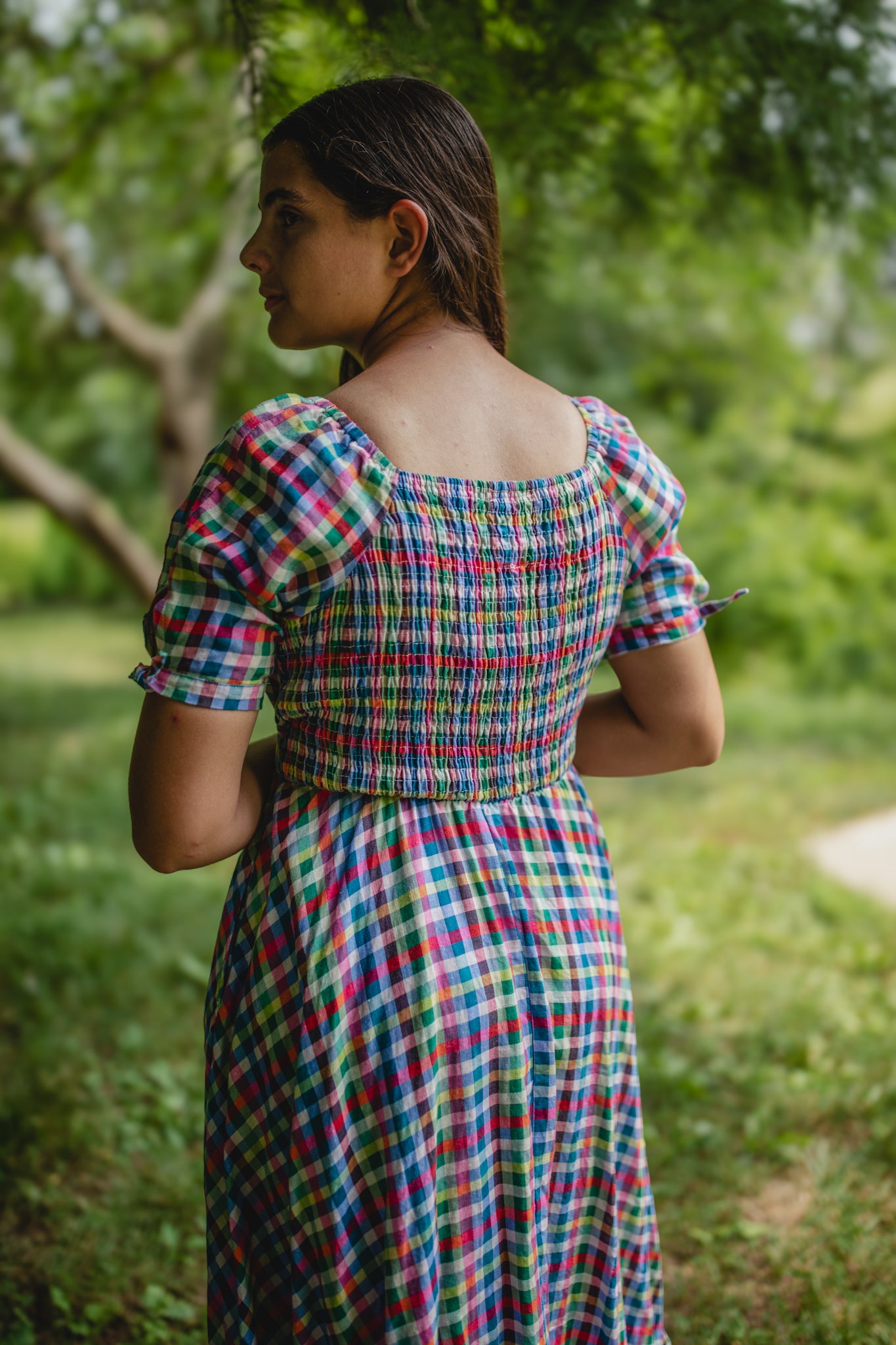 Woman wearing a colorful checkered modest nursing dress standing in a garden.