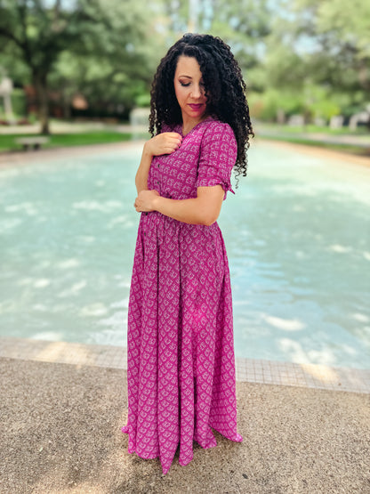 Woman in a pink modest nursing dress standing by a fountain in a park