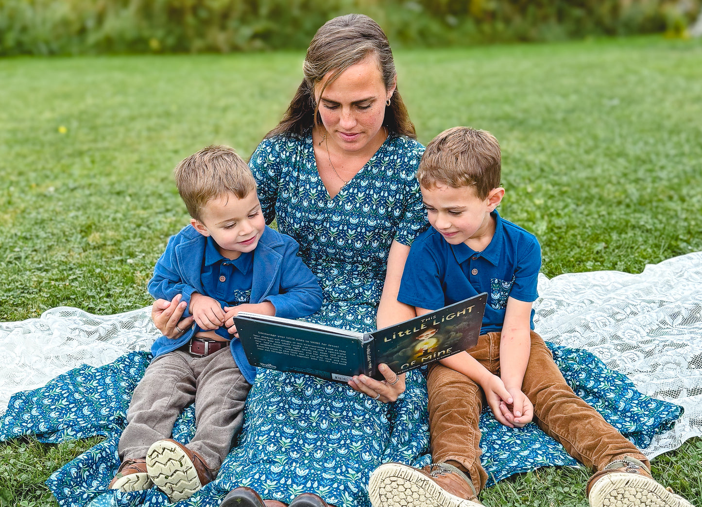Modest nursing mother reading to two children outdoors