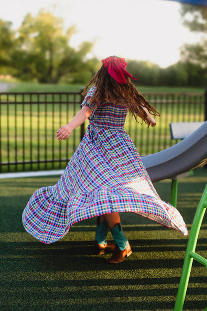 Child in a colorful modest nursing dress with a red headband running on grass with playground equipment in the background