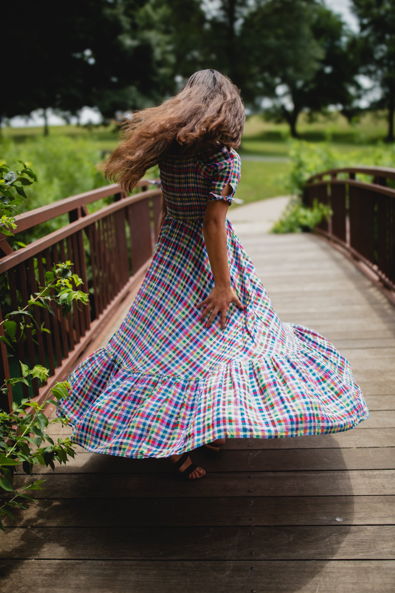 Person in a colorful modest nursing dress walking on a wooden bridge in a natural setting