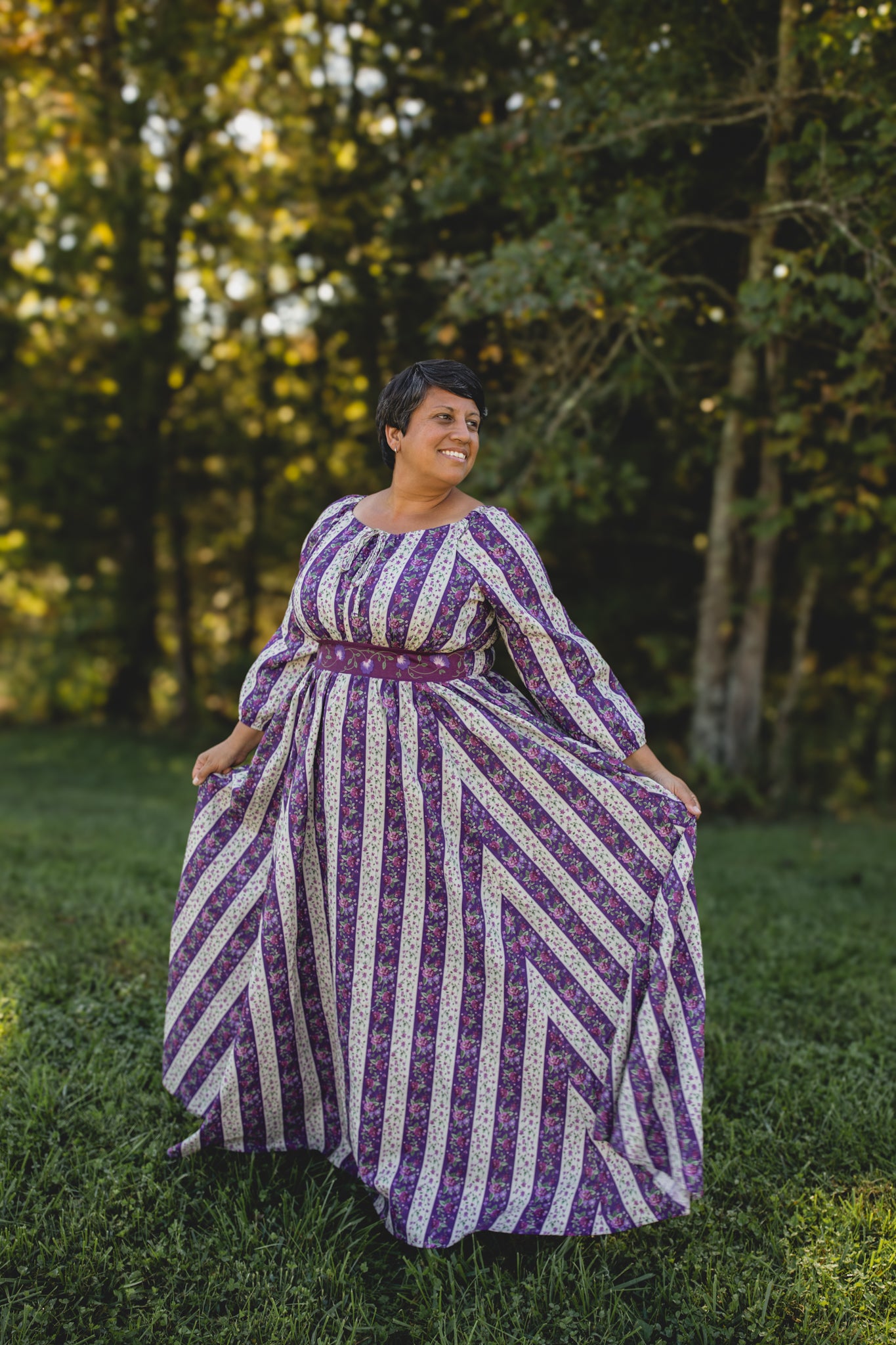 Woman in a modest nursing purple and white patterned dress standing in a forest