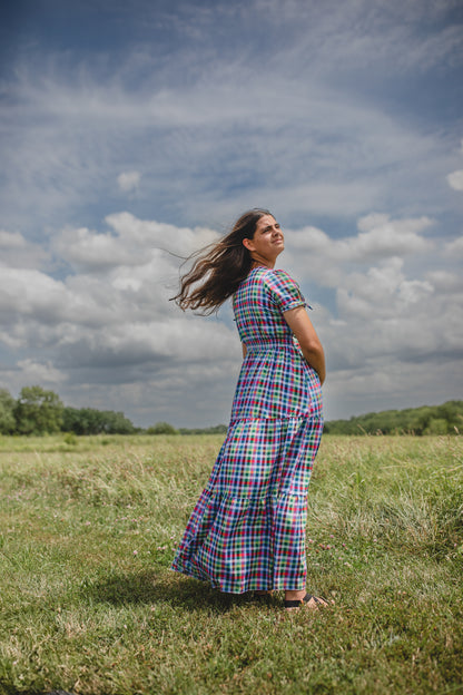 Woman in a plaid modest nursing dress standing in a field with a rainbow in the background