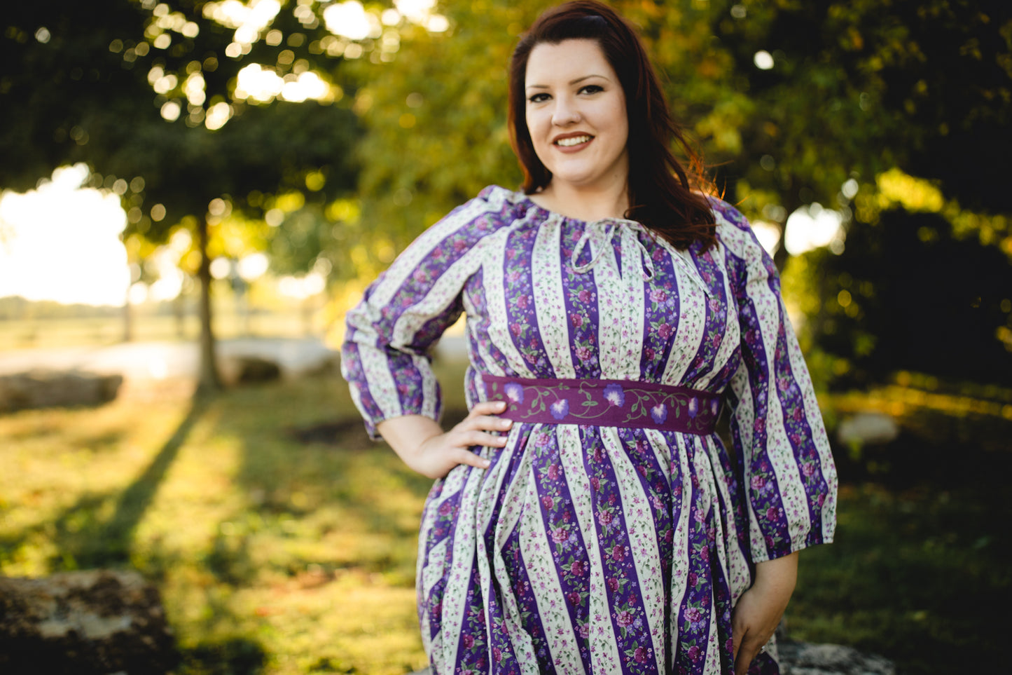 Woman wearing a modest nursing purple and white striped dress standing outdoors with trees in the background
