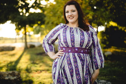 Woman wearing a modest nursing purple and white striped dress standing outdoors with trees in the background