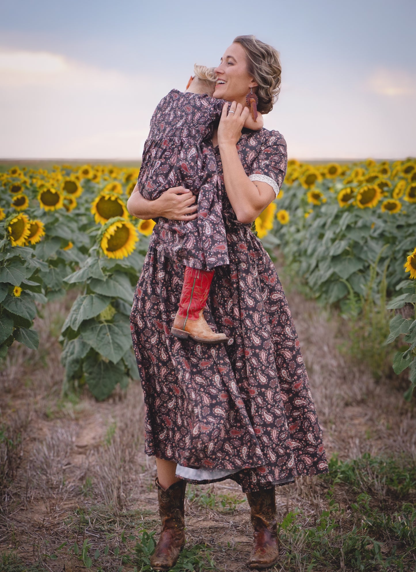 Woman in modest nursing dress holding child in sunflower field