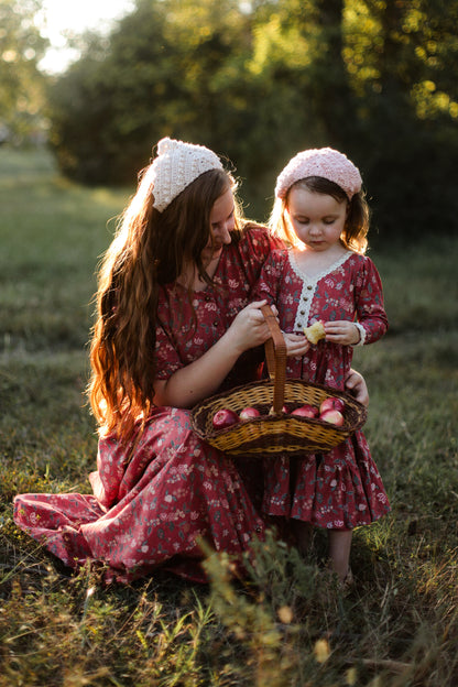 Modest nursing woman and child in matching red floral dresses with apple basket