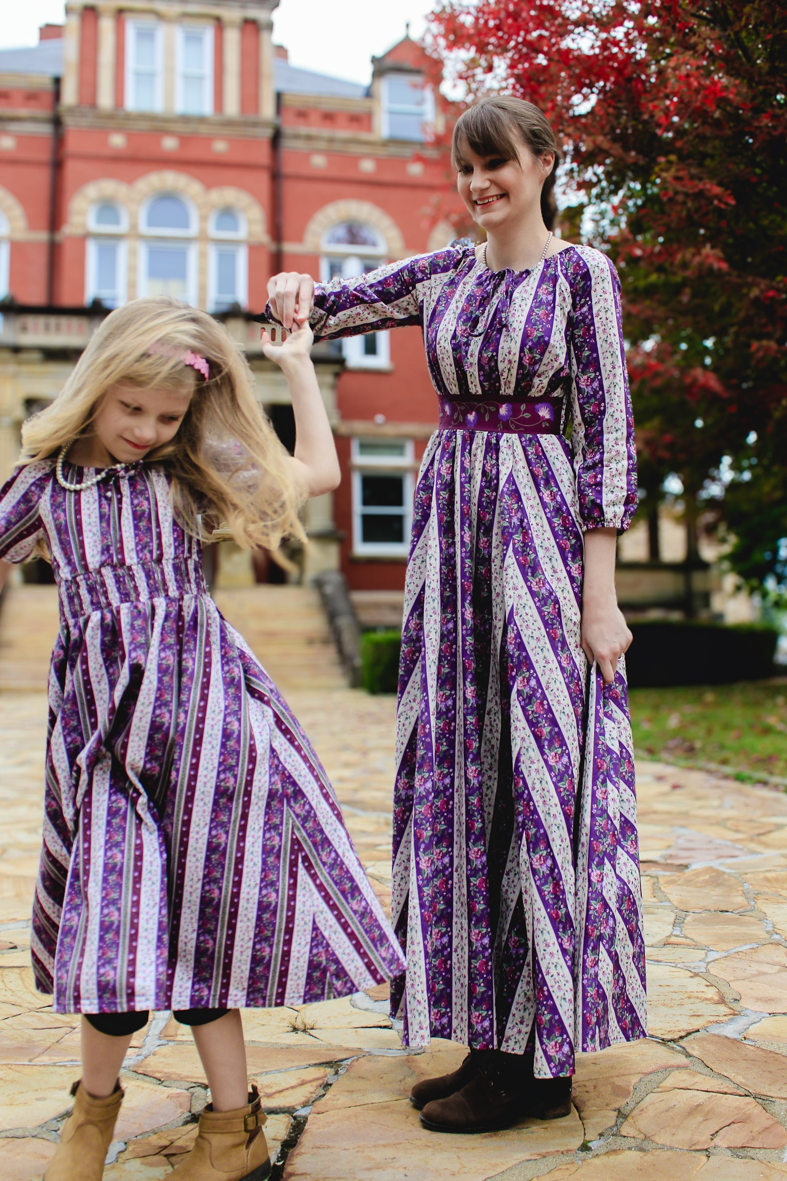 Two women in matching modest purple and white striped dresses standing outdoors.