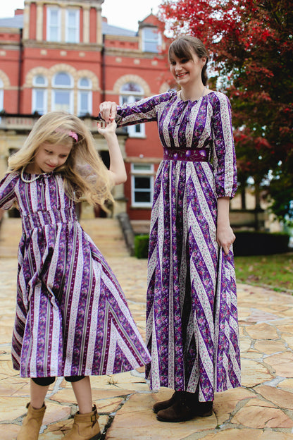Two women in matching modest purple and white striped dresses standing outdoors.