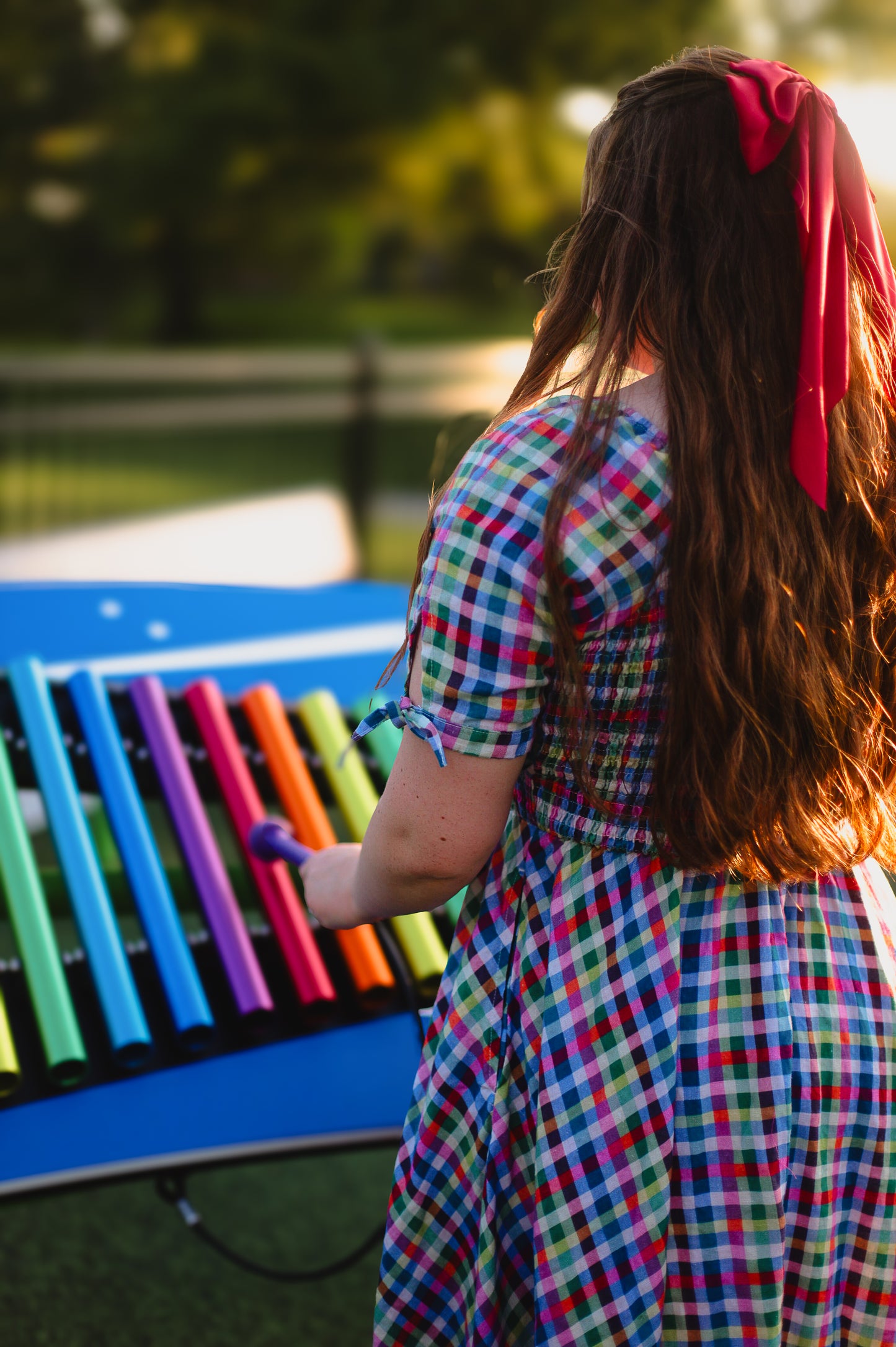 Woman in a colorful modest nursing dress playing a rainbow xylophone outdoors.