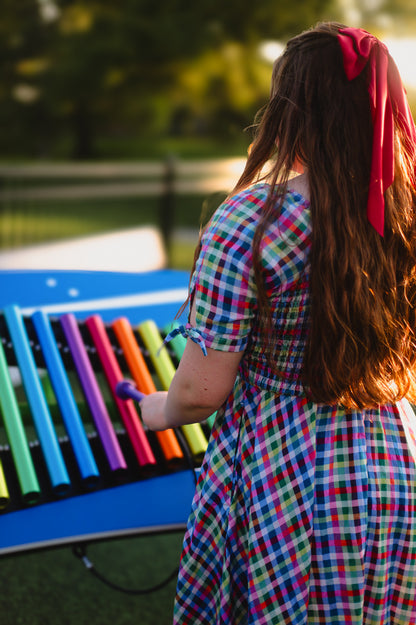 Woman in a colorful modest nursing dress playing a rainbow xylophone outdoors.