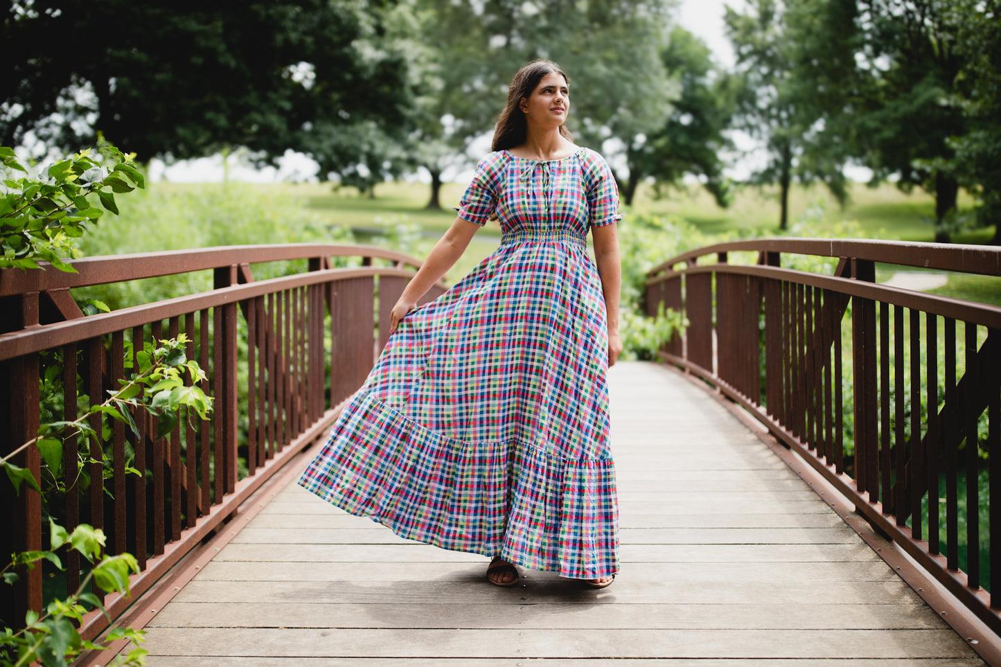 Woman in a colorful modest nursing dress walking on a wooden bridge in a park.