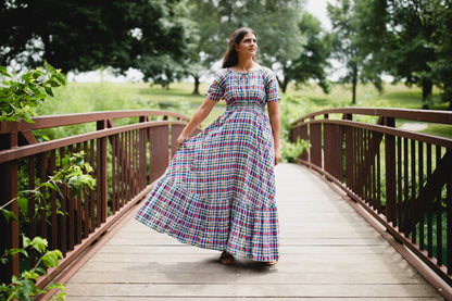 Woman in a colorful modest nursing dress walking on a wooden bridge in a park.