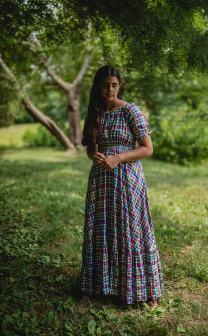 Woman in a colorful modest nursing dress standing in a grassy area with trees in the background