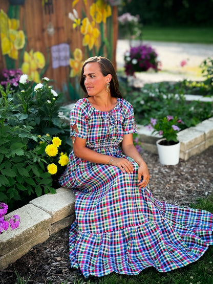 Woman in a colorful modest nursing dress sitting in a garden with flowers and plants around her.