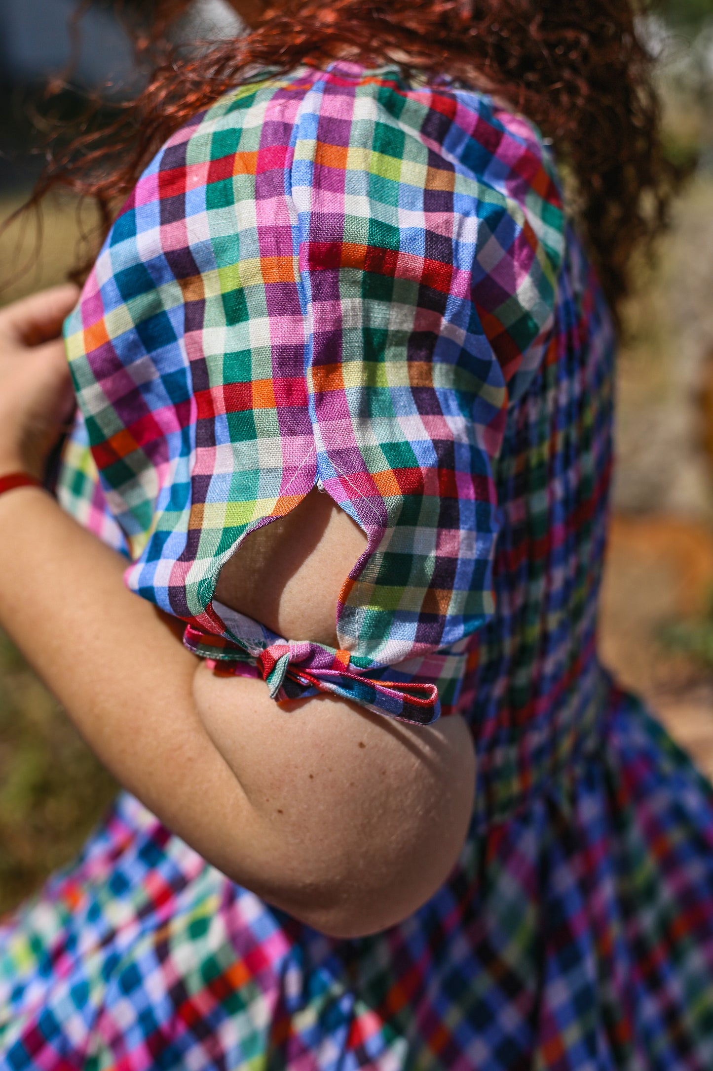 Person wearing a colorful checkered modest nursing dress with a blurred natural background