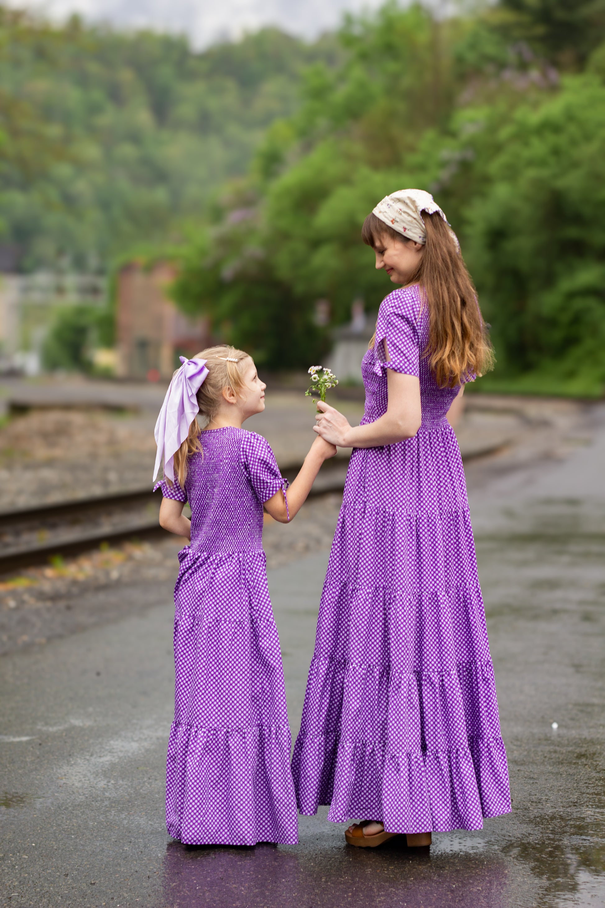 A woman wearing a purple, gingham, five-tiered maxi modest nursing dress with her daughter wearing a matching dress