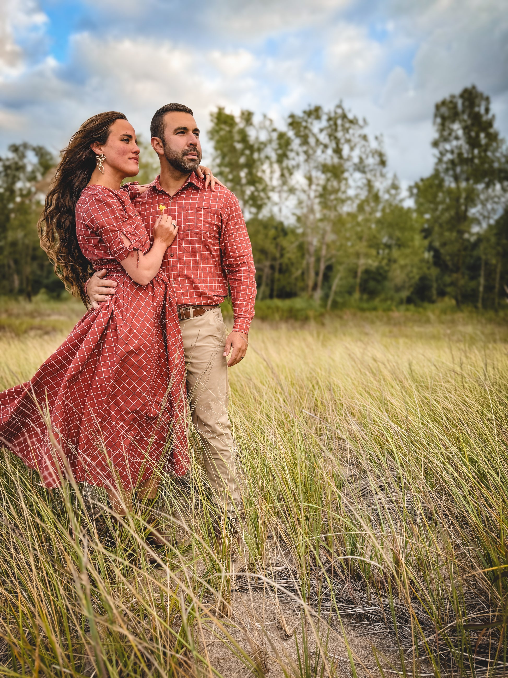 Couple standing in a grassy field with trees in the background