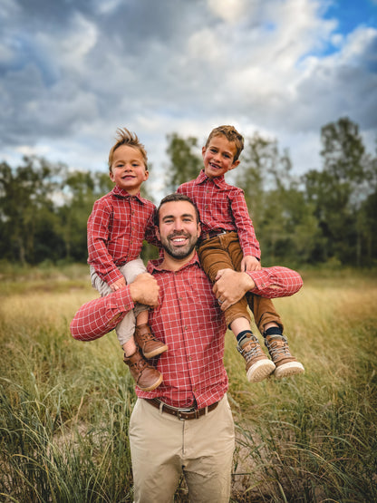 Man with two children on his shoulders in a field with trees and blue sky.
