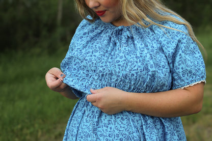 Woman wearing a blue floral modest nursing dress outdoors with a blurred green background