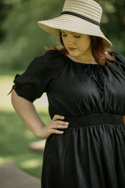 Woman wearing a black modest nursing dress and beige hat outdoors