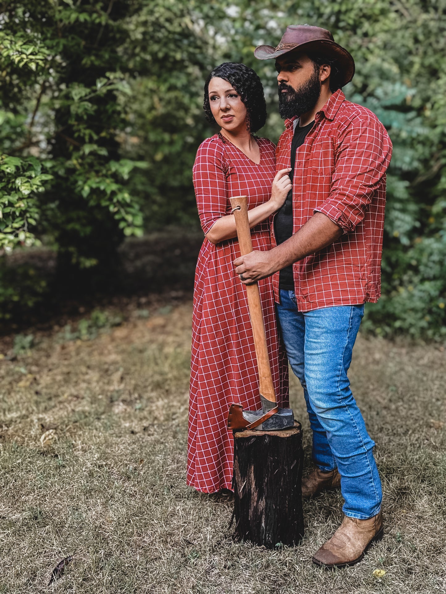 Man and woman wearing modest copper windowpane plaid dresses standing outdoors by chopped wood, showcasing the nursing-friendly design and comfortable cotton blend fabric perfect for family coordinating outfits and outdoor activities