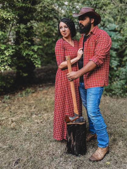 Man and woman wearing modest copper windowpane plaid dresses standing outdoors by chopped wood, showcasing the nursing-friendly design and comfortable cotton blend fabric perfect for family coordinating outfits and outdoor activities