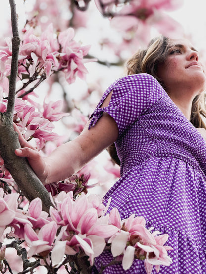 A woman wearing a purple, gingham, five-tiered maxi modest nursing dress