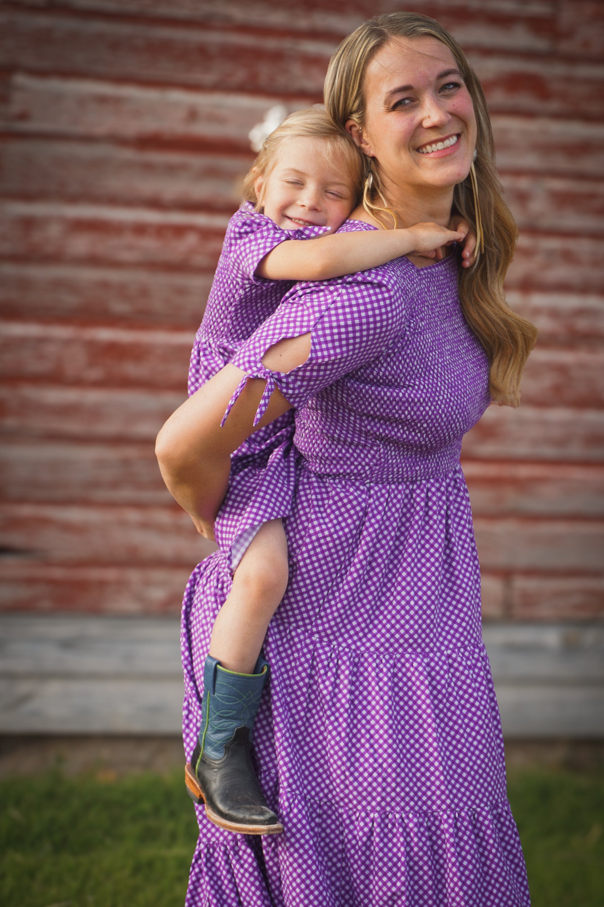 A woman wearing a purple, gingham, five-tiered maxi modest nursing dress with her daughter wearing a matching dress