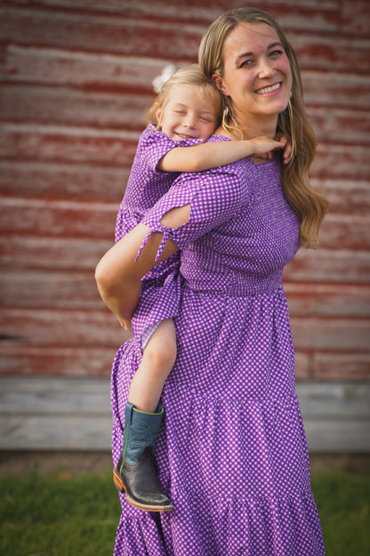 A woman wearing a purple, gingham, five-tiered maxi modest nursing dress with her daughter wearing a matching dress