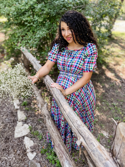 Woman in a colorful modest nursing dress standing outdoors near a wooden fence with greenery in the background
