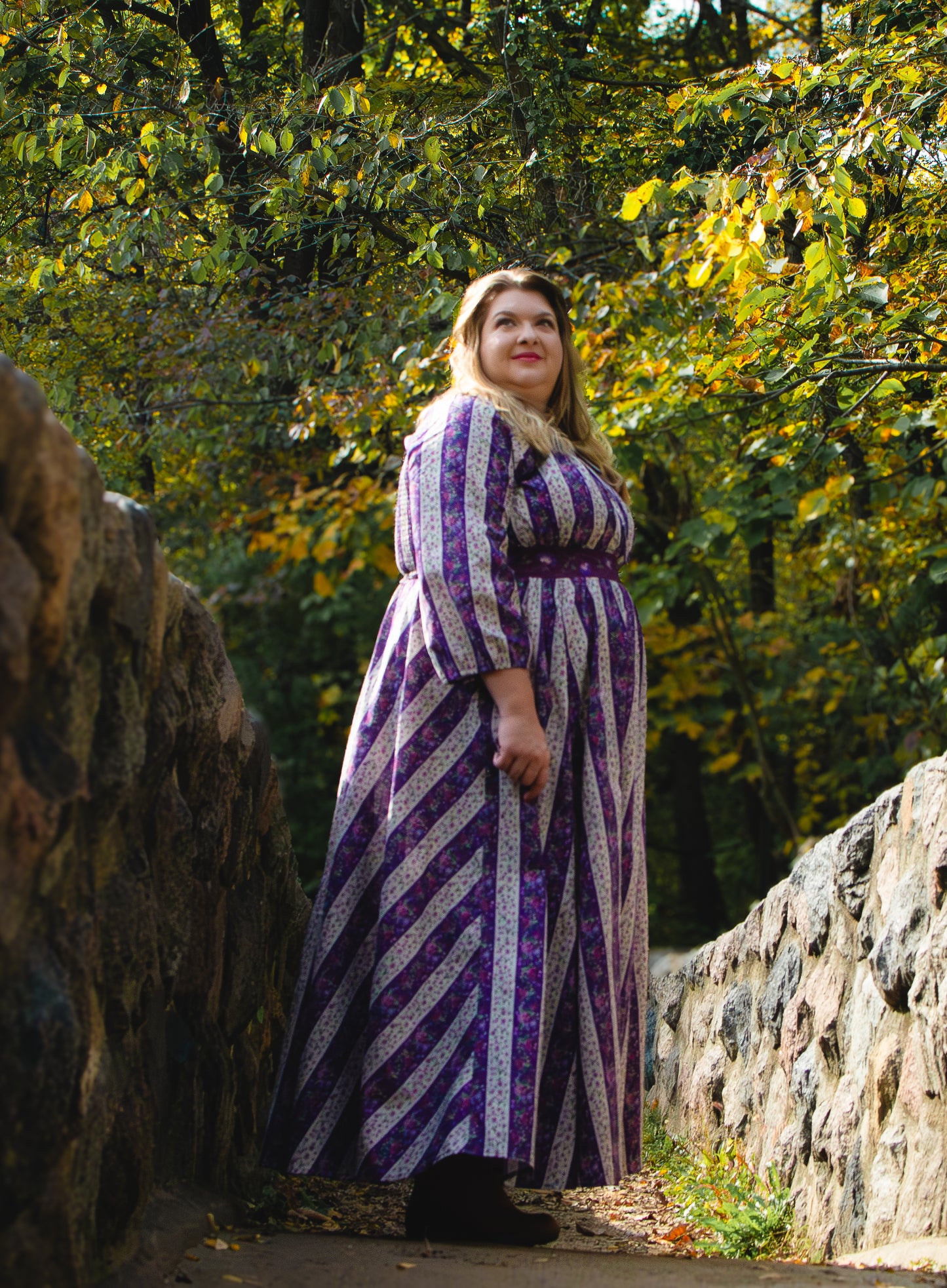 Woman in a modest nursing long, patterned dress standing outdoors with trees in the background