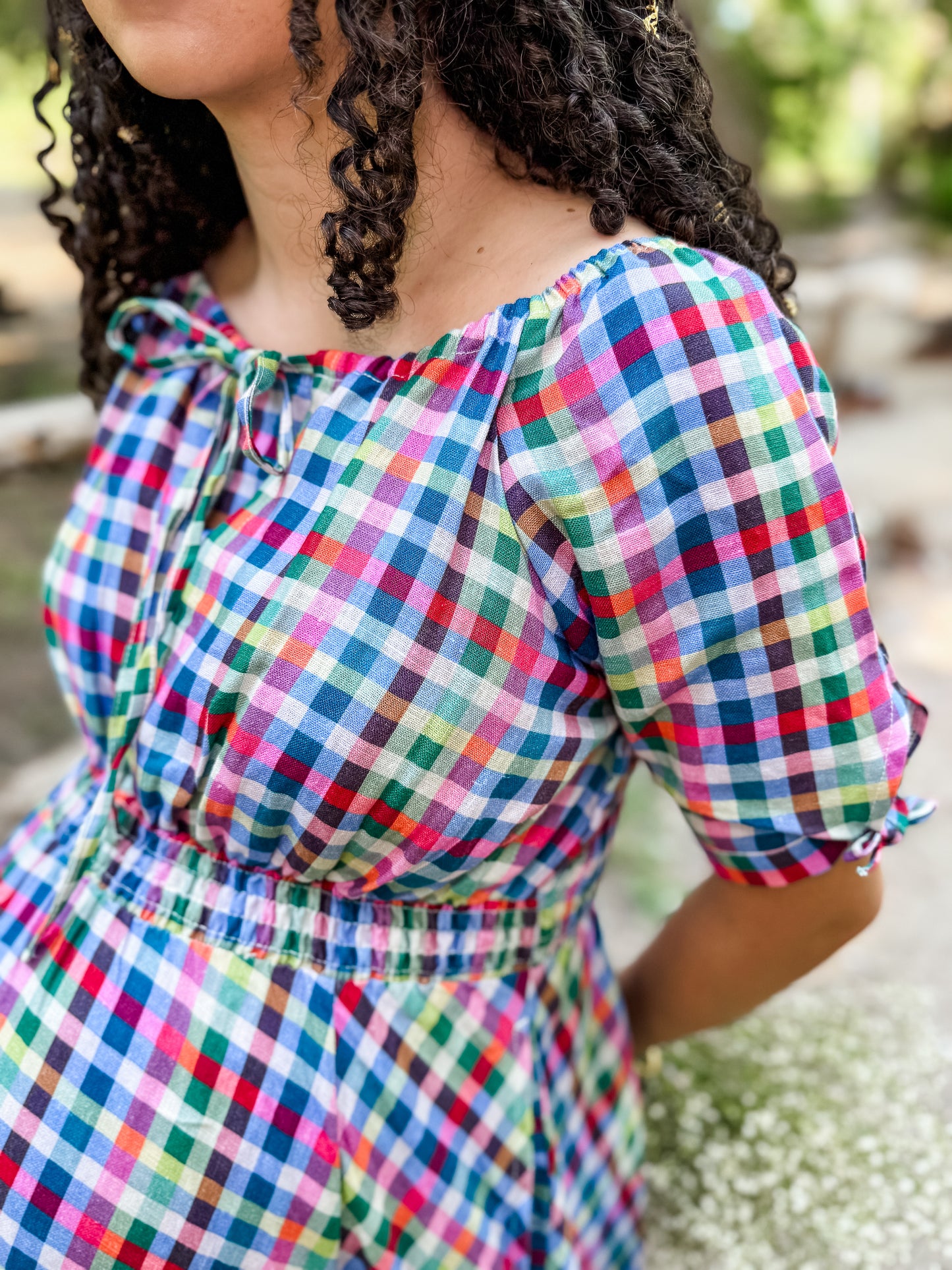 Person wearing a colorful checkered modest nursing dress with a blurred natural background