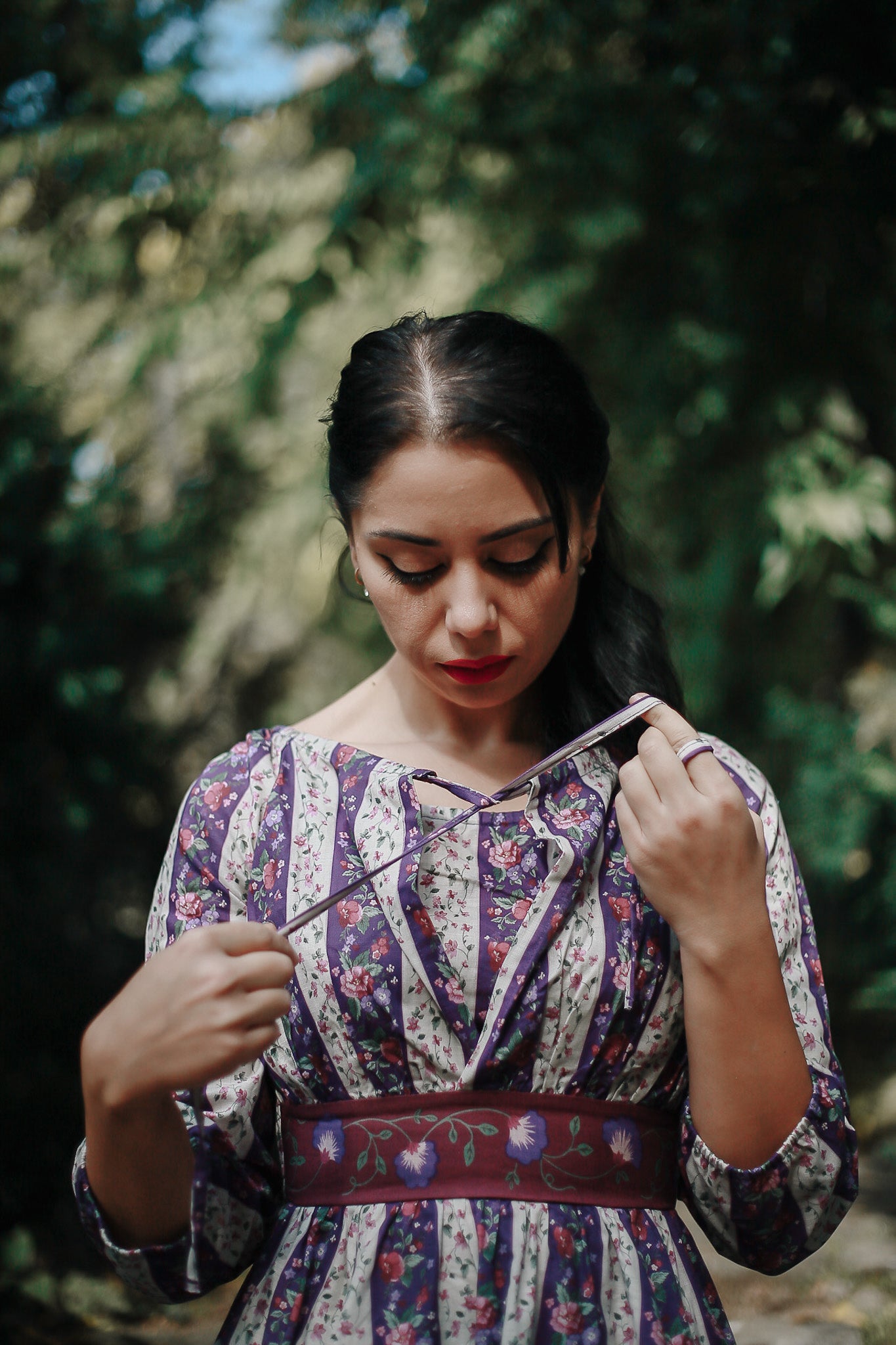 Woman in a patterned modest nursing dress holding a small object in a forest setting