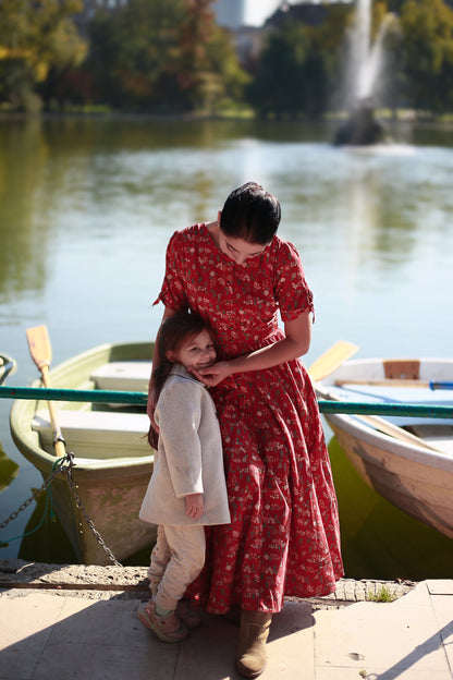 Woman in modest nursing red dress holding child by lake
