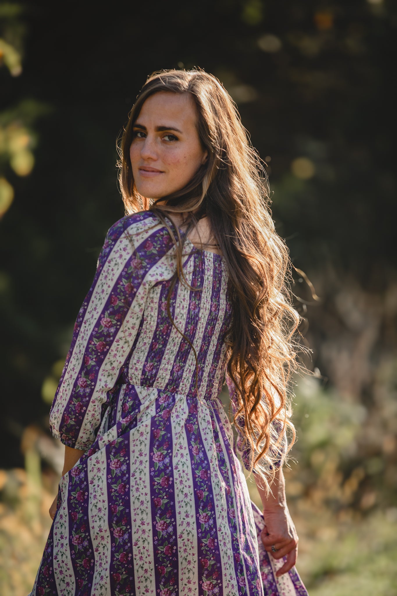 Woman in a striped modest nursing dress standing outdoors with trees in the background