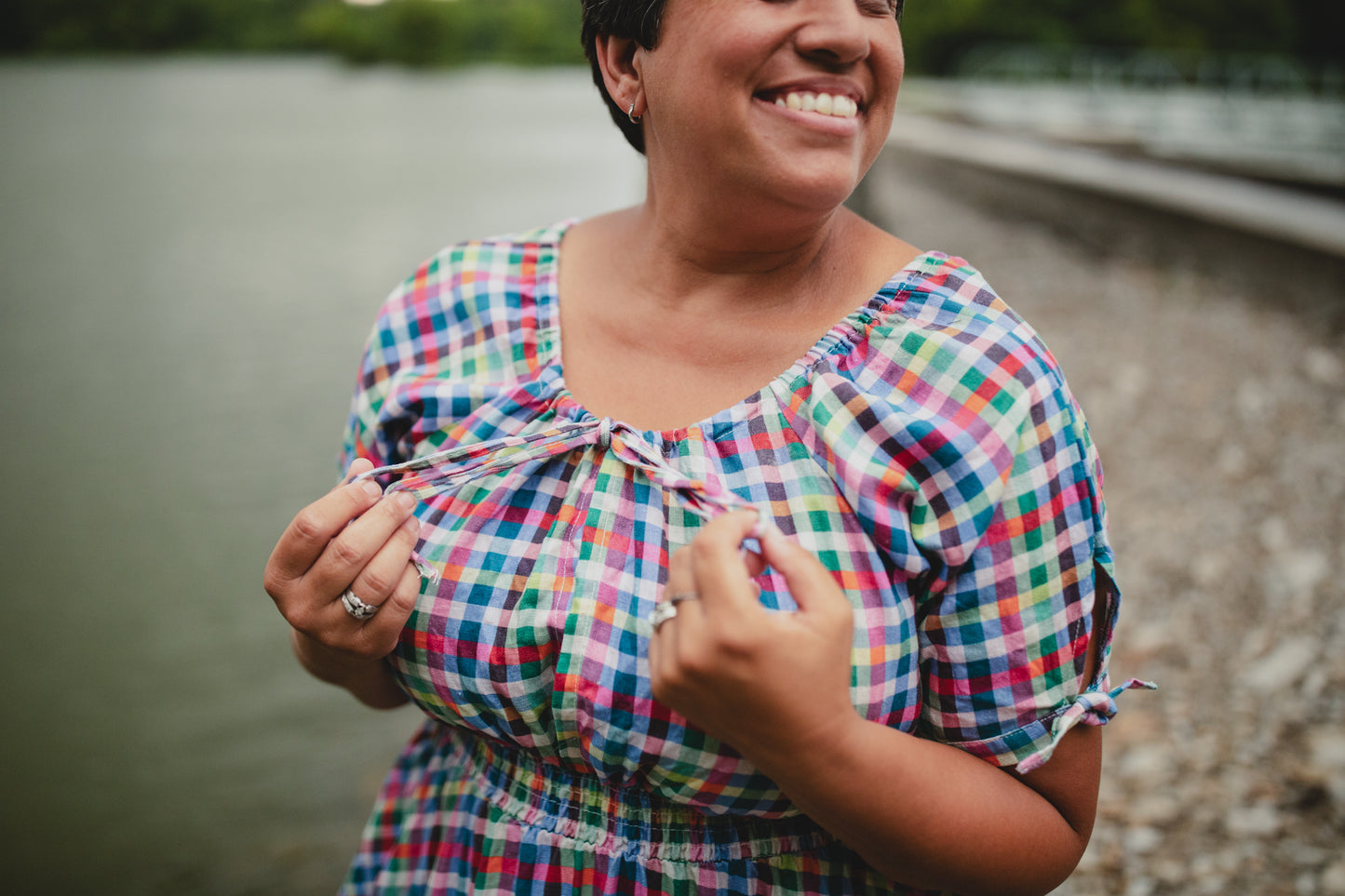 Woman in a colorful checkered modest nursing dress standing by a body of water.