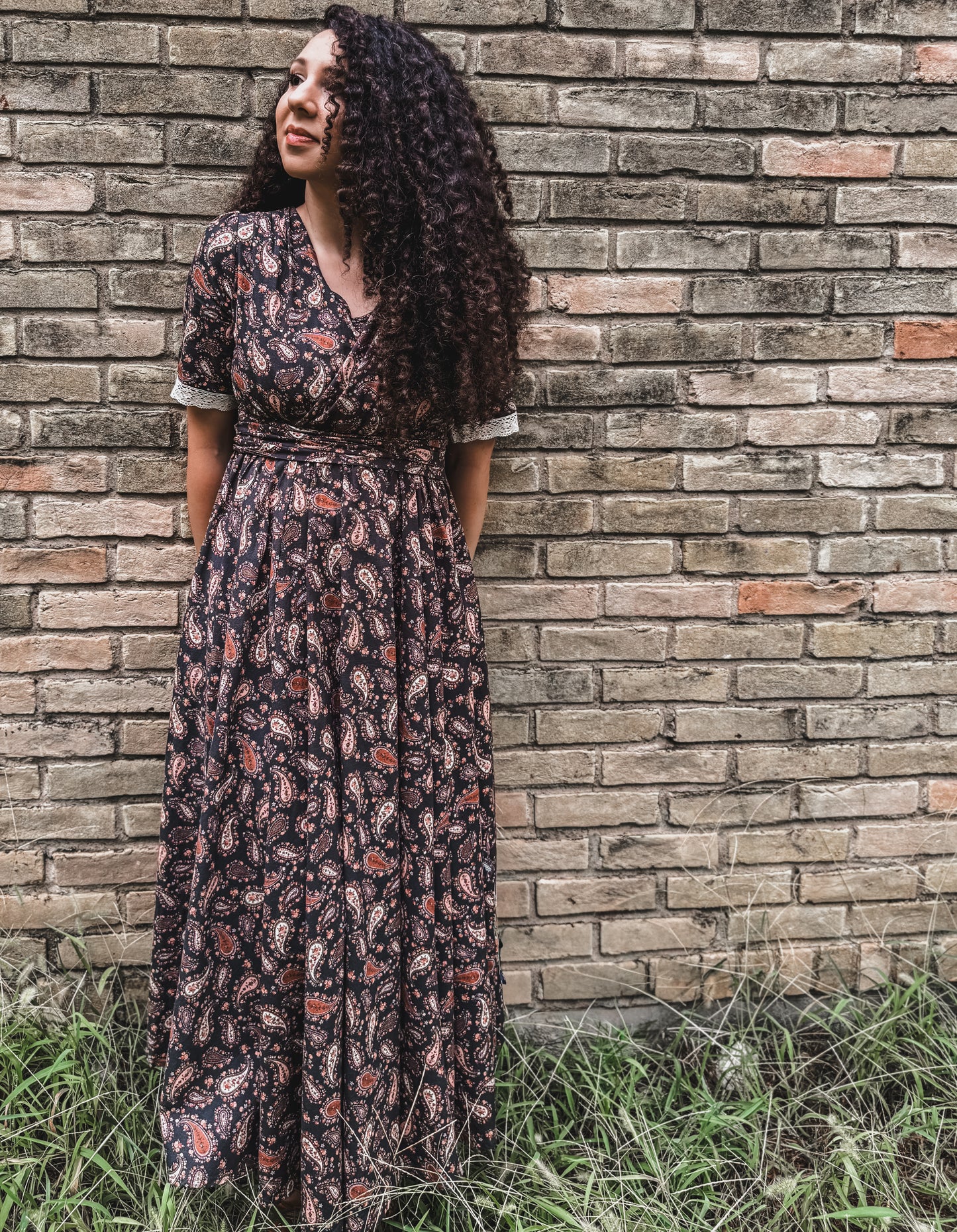 Woman in modest nursing floral dress against brick wall