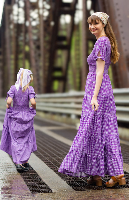A woman wearing a purple, gingham, five-tiered maxi modest nursing dress with her daughter wearing a matching dress