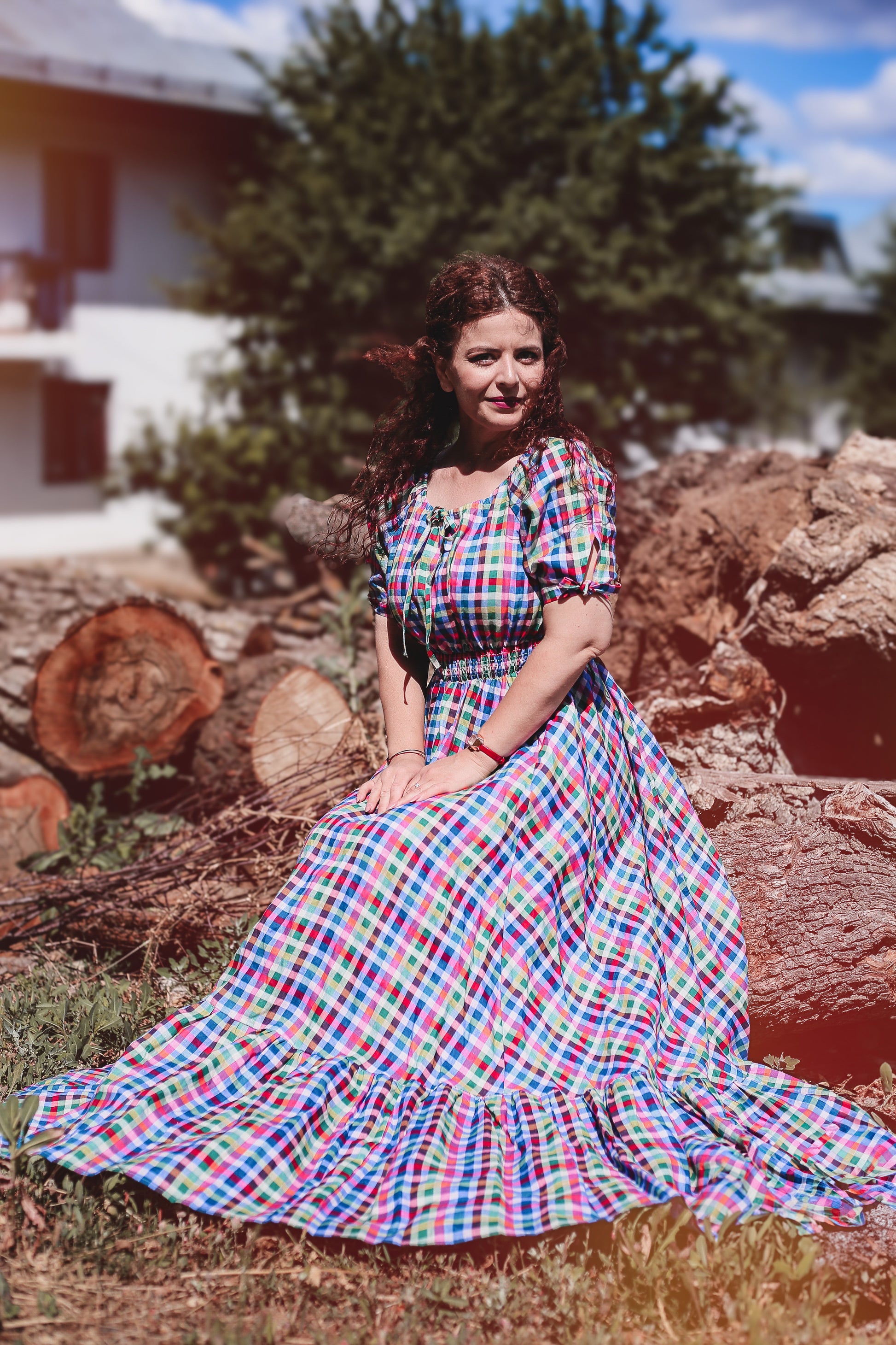 Woman in a colorful modest nursing dress sitting among logs with a blurred background