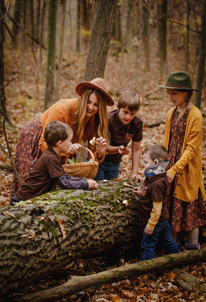 Mother in modest nursing dress with children playing on forest logs