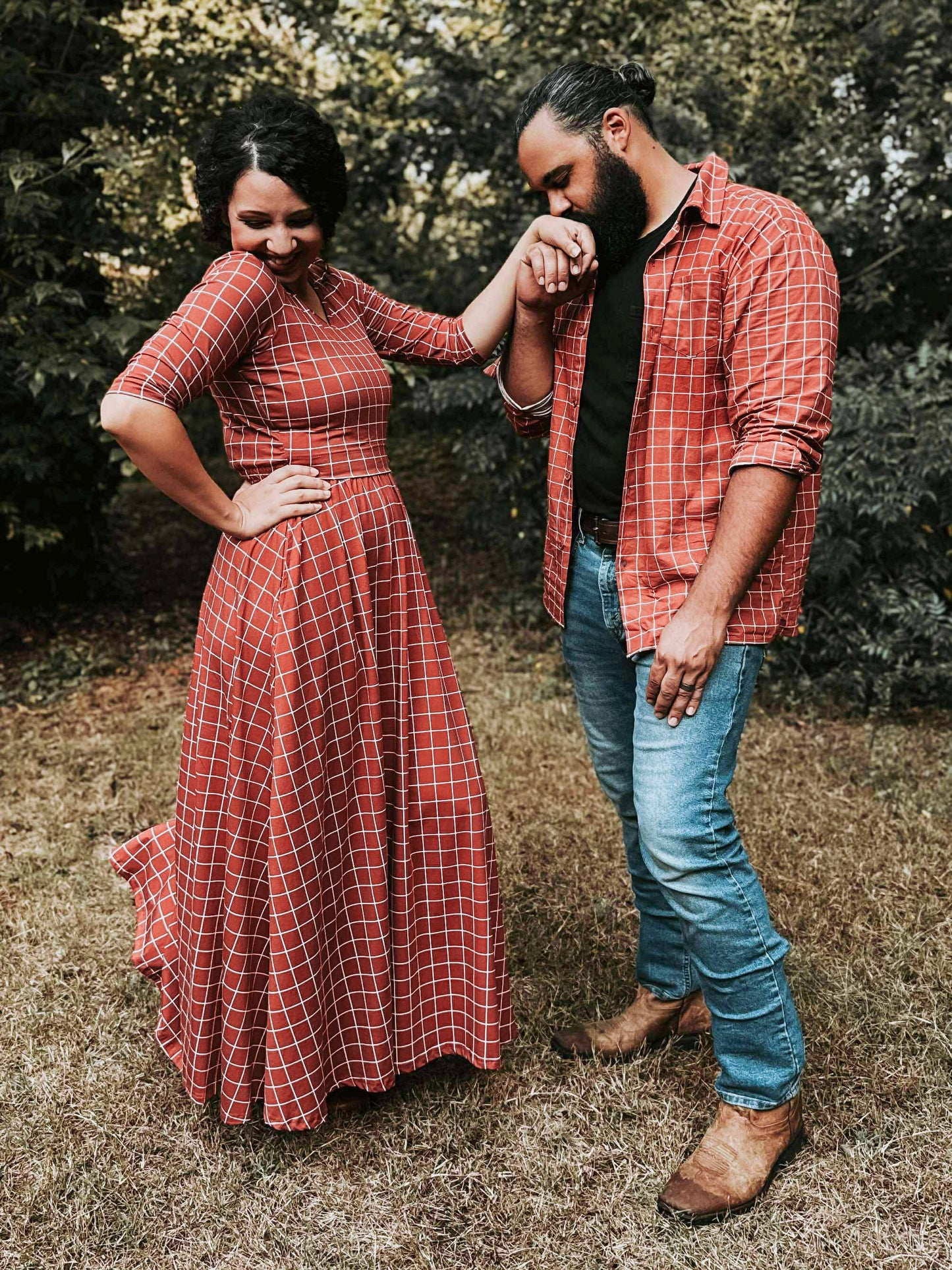 Couple in matching red plaid outfits standing outdoors.