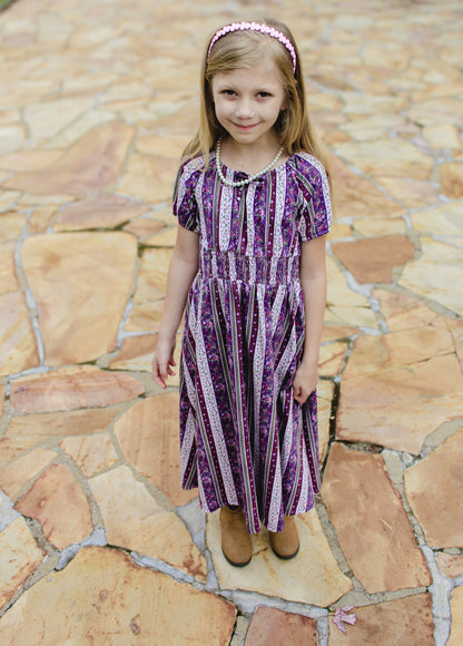Young girl in a purple dress standing on a stone pavement